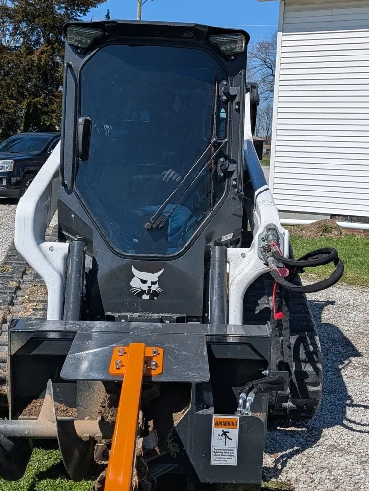 Close view of a Bobcat compact track loader with an orange attachment parked beside a home